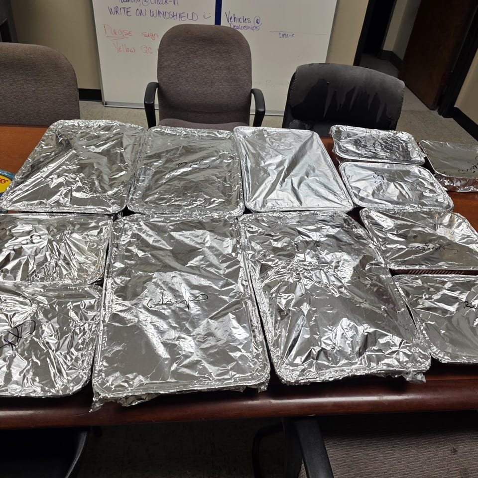 Numerous foil-covered catering trays of halal food on a wooden table, ready for delivery.