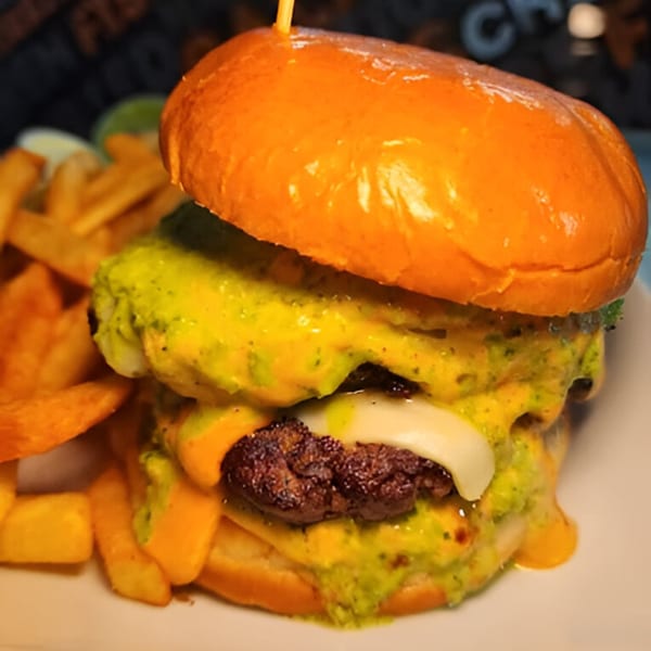 A double halal cheeseburger with melted cheese and green sauce, served with golden french fries.